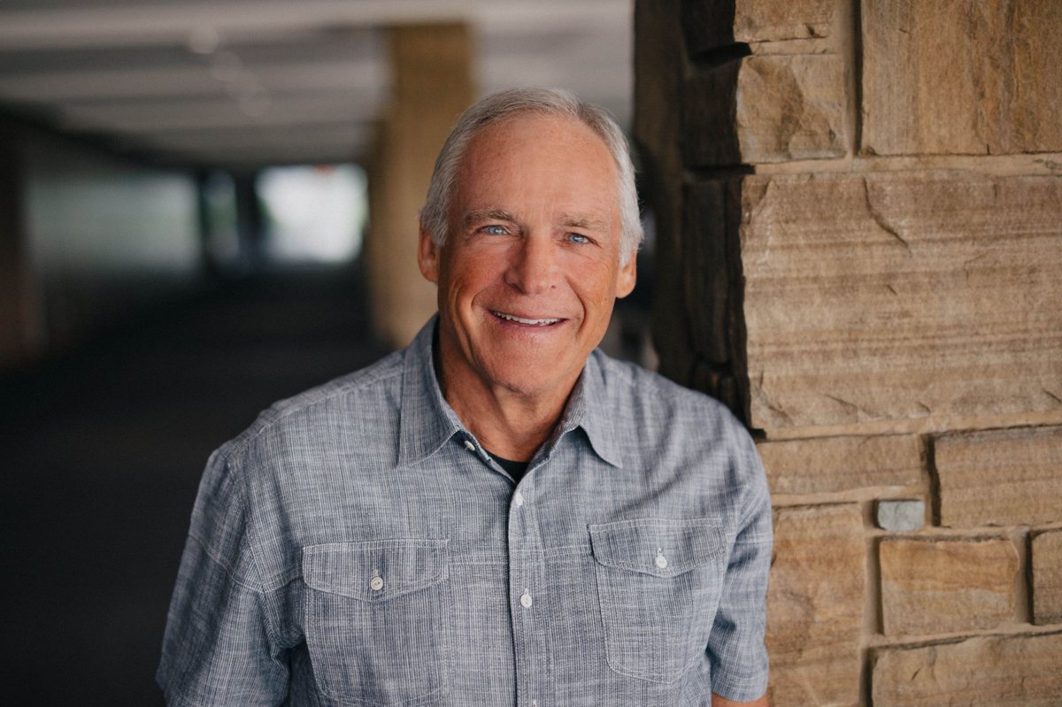 Tom Lane smiling, leaning against a stone pillar